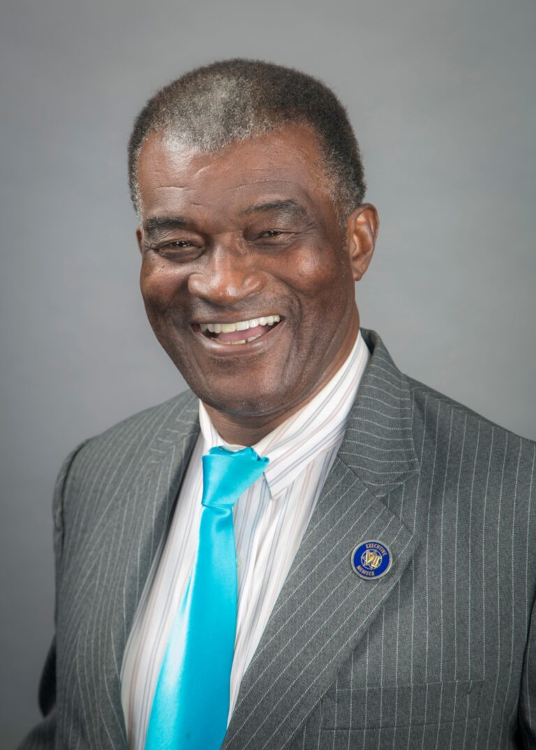 Coach Jim Foster smiling in a gray pinstripe suit and teal tie
